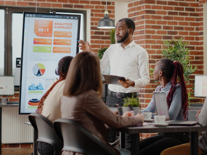 Company employee presenting business strategy with charts on monitor, planning project. Workmates analyzing financial statistics on display, working together on company development.